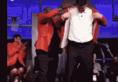 A Man In An Orange Jacket Is Being Lifted By Another Man In A White Shirt GIF
