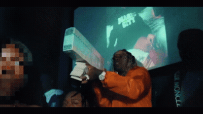 A Man In An Orange Jacket Is Holding A Large Stack Of Money In Front Of A Screen That Says Miami City GIF