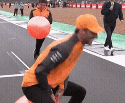 A Man In An Orange Jacket Is Holding An Orange Ball On A Track GIF