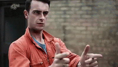 A Man In An Orange Jacket Is Making A Funny Face And Pointing At The Camera . GIF