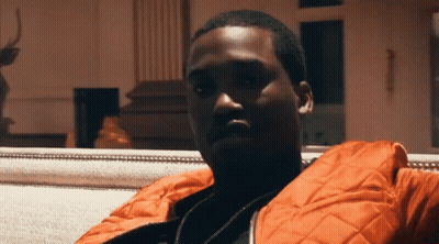 A Man In An Orange Jacket Sits On A White Couch GIF