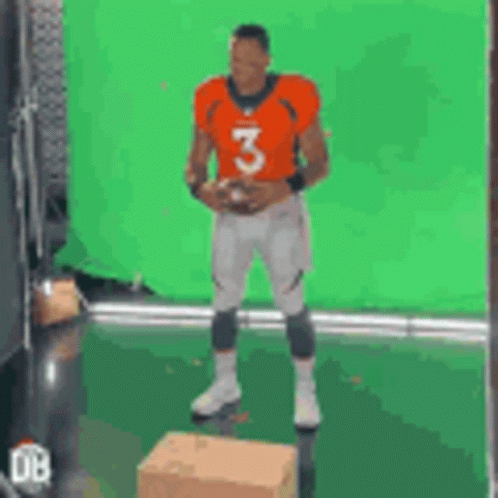 A Man In An Orange Jersey With The Number 3 Is Holding A Football . GIF