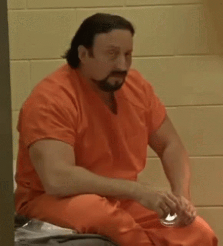 A Man In An Orange Jumpsuit Is Sitting On A Bed In A Prison Cell . GIF