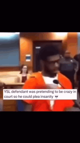 A Man In An Orange Jumpsuit Is Talking Into A Microphone In A Courtroom . GIF