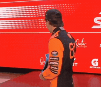 A Man In An Orange Shirt And Hat Is Holding A Trophy In Front Of A Red Background . GIF