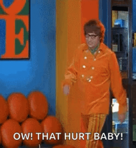 A Man In An Orange Shirt And Striped Pants Is Standing In Front Of A Bunch Of Pumpkins In A Room . GIF