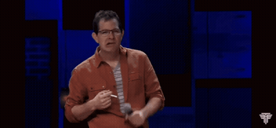 A Man In An Orange Shirt And Tie Is Holding A Microphone In His Hand GIF