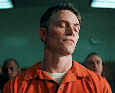 A Man In An Orange Shirt Has His Eyes Closed And Has A Scar On His Face GIF
