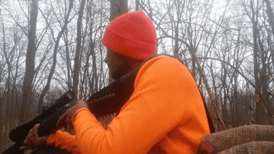 A Man In An Orange Shirt Holds A Rifle GIF