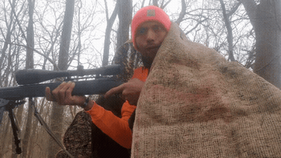 A Man In An Orange Shirt Is Holding A Rifle And Pointing GIF