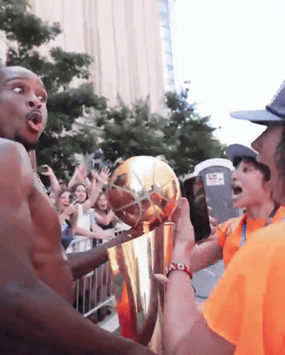 A Man In An Orange Shirt Is Holding A Trophy In Front Of A Crowd Of People GIF
