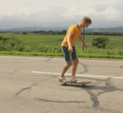 A Man In An Orange Shirt Is Riding A Skateboard Down The Road GIF