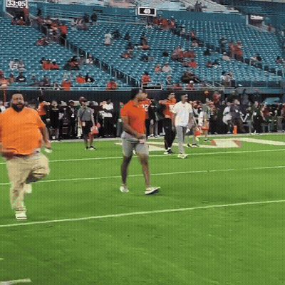 A Man In An Orange Shirt Is Running On A Football Field With A Sign That Says 40 On It GIF