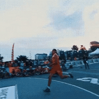 A Man In An Orange Shirt Is Running On A Track With The Number 3 On It GIF