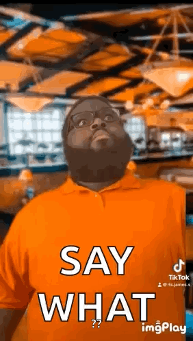 A Man In An Orange Shirt Is Saying `` Say What '' . GIF