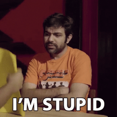 A Man In An Orange Shirt Is Sitting At A Table With His Arms Crossed And Says `` I 'M Stupid '' GIF