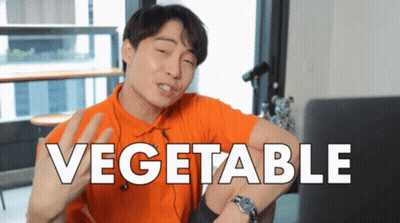 A Man In An Orange Shirt Is Sitting In Front Of A Laptop With The Word Vegetable On The Screen GIF
