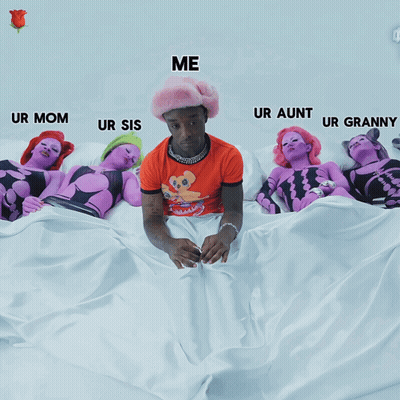 A Man In An Orange Shirt Is Sitting On A Bed Surrounded By Purple Women GIF