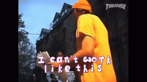 A Man In An Orange Shirt Is Standing In Front Of A Building With The Words " I Can 'T Work Like This " Written On It GIF