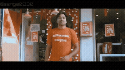 A Man In An Orange Shirt Is Standing In Front Of A Store With A Sign That Says 50 % Off . GIF
