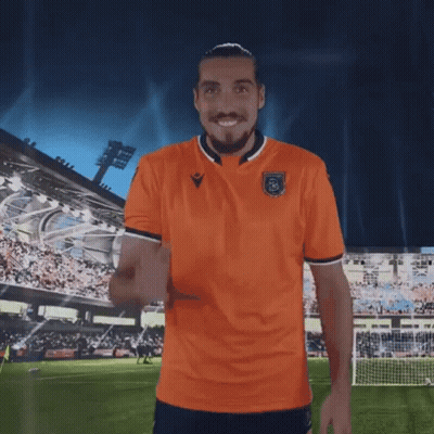 A Man In An Orange Shirt Is Standing On A Soccer Field With His Arms Outstretched GIF