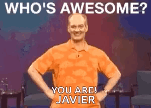 A Man In An Orange Shirt Is Standing With His Hands On His Hips And Smiling . GIF