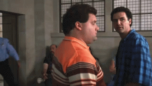 A Man In An Orange Shirt Is Talking To Another Man GIF