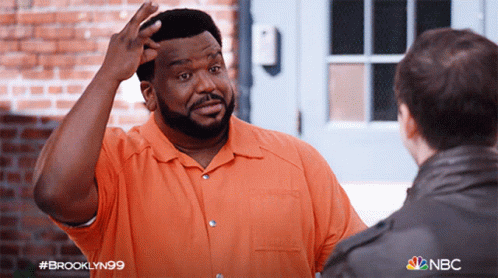 A Man In An Orange Shirt Is Talking To Another Man In A Brooklyn99 Advertisement GIF