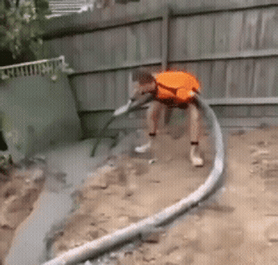A Man In An Orange Shirt Is Using A Hose To Pump Concrete Into The Ground . GIF
