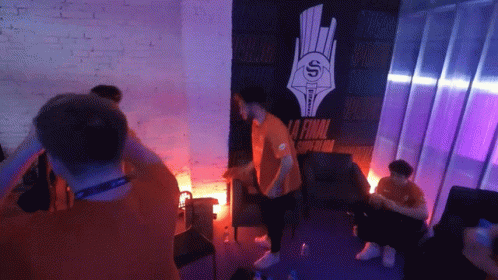 A Man In An Orange Shirt Stands In Front Of A Wall That Says La Final GIF