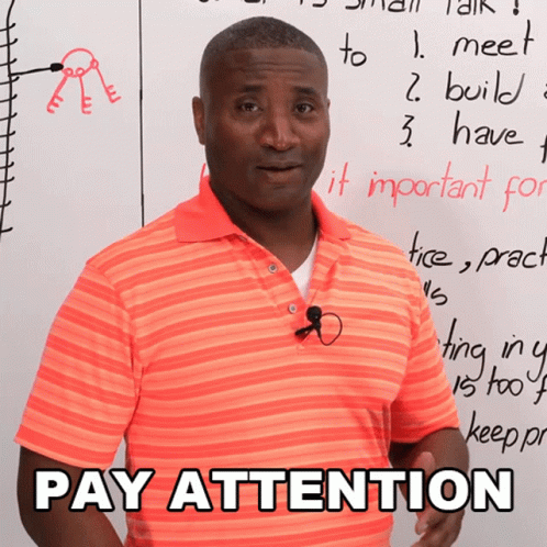 A Man In An Orange Shirt Stands In Front Of A White Board With Pay Attention Written On It GIF