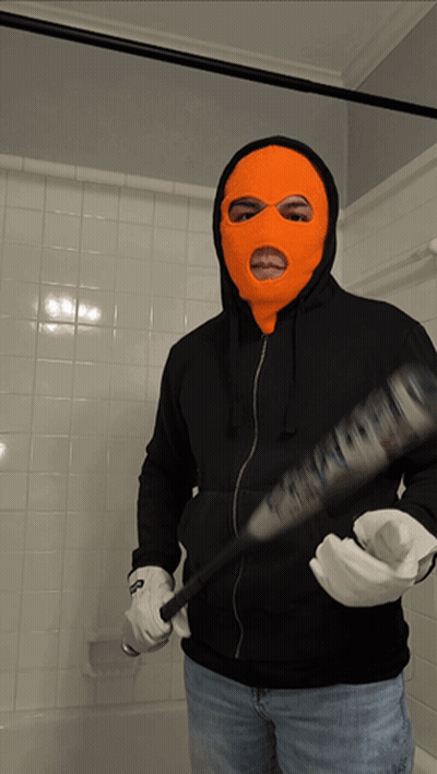 A Man In An Orange Ski Mask Is Holding A Bat GIF