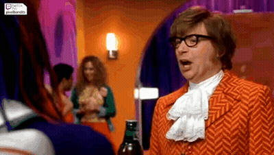 A Man In An Orange Suit And Glasses Is Standing In A Room Talking To A Woman . GIF