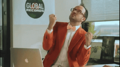A Man In An Orange Suit Is Sitting In Front Of An Apple Laptop In Front Of A Global Records Sign GIF