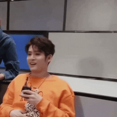 A Man In An Orange Sweater Is Holding A Cell Phone In His Hand And Smiling . GIF