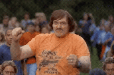 A Man In An Orange T-Shirt With A Gun On It Is Dancing In Front Of A Crowd . GIF