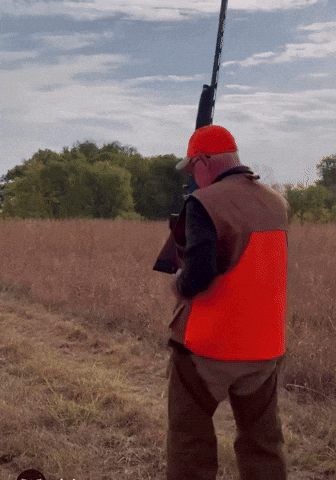 A Man In An Orange Vest Is Holding A Gun GIF