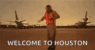 A Man In An Orange Vest Is Standing On A Runway In Front Of Planes . GIF