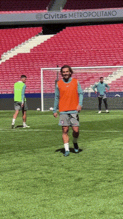 A Man In An Orange Vest Is Walking On A Soccer Field In Front Of A Sign That Says Civitas Metropolitano GIF