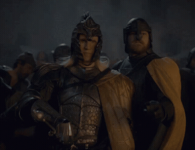 A Man In Armor Holding A Sword Stands Next To Another Man GIF