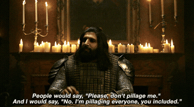 A Man In Armor Is Sitting At A Table With Candles Behind Him GIF