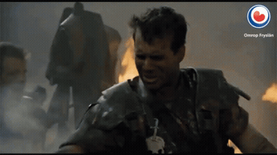A Man In Armor Is Smiling In Front Of A Fire And A Sign That Says Omrop Frysian GIF