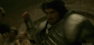 A Man In Armor Is Standing In Front Of A Group Of People In A Dark Room . GIF