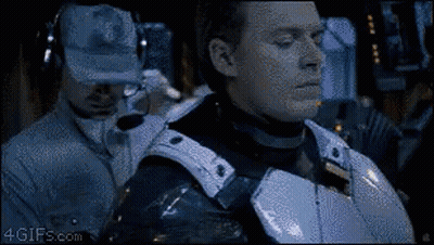 A Man In Armor Is Standing Next To A Man Wearing A Hat And Headphones . GIF