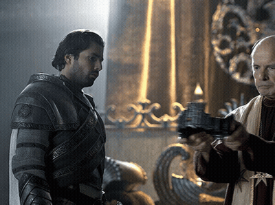 A Man In Armor Is Standing Next To Another Man Who Is Holding A Gun GIF