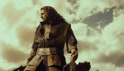 A Man In Armor Is Standing On Top Of A Hill Holding A Sword . GIF