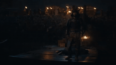 A Man In Armor Stands In Front Of A Crowd Of People Holding A Sword GIF