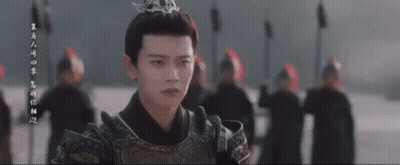 A Man In Armor With A Crown On His Head Is Standing In Front Of A Group Of People . GIF