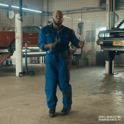 A Man In Blue Overalls Is Dancing In A Garage GIF