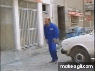 A Man In Blue Overalls Is Walking Down The Street Next To A White Car GIF